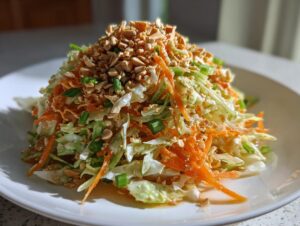 A beautifully plated mound of asian cabbage salad featuring shredded cabbage, carrots, and green onions, generously topped with chopped peanuts.