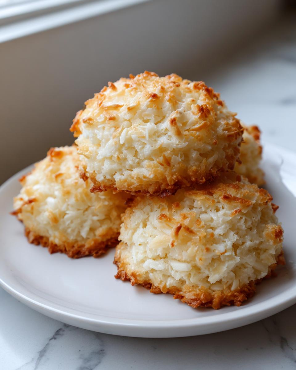A stack of three perfectly baked, golden brown coconut cookies with crispy edges.