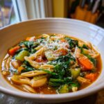 A close-up of a steaming bowl of minestrone soup, rich with vegetables, pasta, and topped with grated Parmesan cheese.