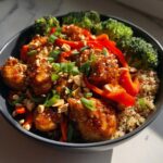 Close-up of a high-protein peanut chicken meal prep bowl with quinoa, roasted broccoli, and red peppers.