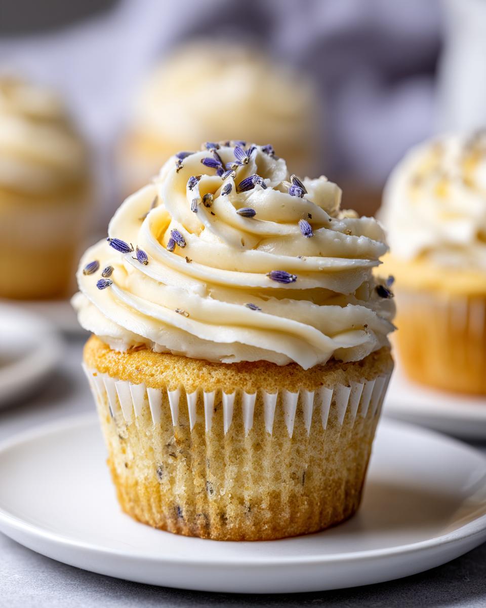 A single, perfectly frosted lavender honey cupcake topped with dried lavender buds, sitting on a white plate.