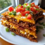 Close-up of a layered slice of mexican pizza with melted cheese, seasoned beef, tomatoes, and green onions.