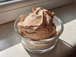 A scoop of light brown, airy lebanese date blossom mousse served in a small clear glass bowl.