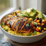 Close-up of lemon chili grilled chicken bowls featuring sliced seasoned chicken over yellow quinoa, black beans, corn, and avocado.