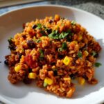 A close-up of a serving of vibrant mexican chorizo rice mixed with black beans, corn kernels, and topped with fresh cilantro.