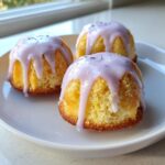 Three individual mini lemon cakes topped with dripping lavender glaze and sprinkled with dried lavender.