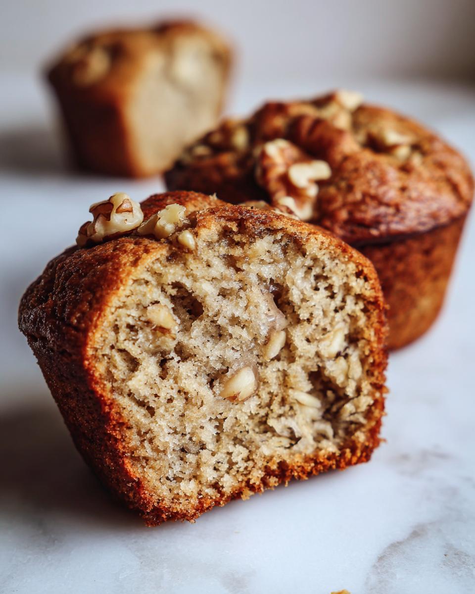 Close-up of a moist banana nut muffin cut in half, showing walnuts inside and on top.