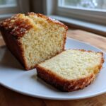 A close-up of a slice cut from a loaf of moist cream cheese pound cake on a white plate.
