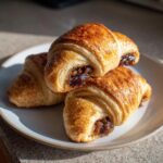 Three golden-brown pecan pie crescents stacked on a light plate, showing the rich pecan filling.
