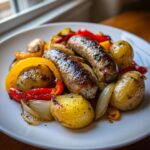 Close-up of a white plate featuring two browned sausages with roasted potatoes, peppers, and onions, a perfect sausage peppers onions and potatoes dish.