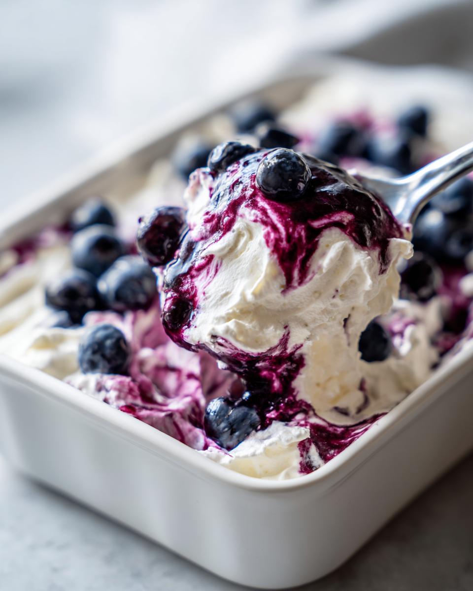 A spoonful of creamy blueberry fluff salad topped with blueberry sauce and fresh blueberries being lifted from a white dish.