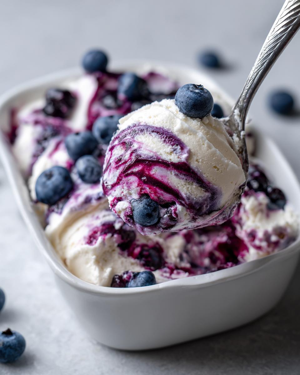 A metal spoon scoops a portion of creamy white blueberry fluff salad swirled with blueberry sauce and topped with fresh blueberries.