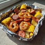 Close-up of cooked shrimp and sausage foil packs with corn on the cob and potatoes.
