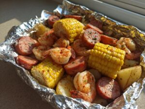 Close-up of cooked shrimp and sausage foil packs featuring corn on the cob and potatoes seasoned with spices.
