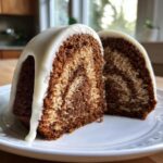 A close-up of two slices of marbled sock-it-to-me cake topped with thick white glaze dripping down the sides.