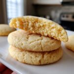 Close-up of stacked sourdough sugar cookies, one broken open to show the soft, crumbly interior texture.