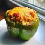 Close-up of a single, bright green southern stuffed bell peppers topped with melted, golden-brown cheese.