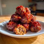 A pile of juicy sriracha honey glazed meatballs on a white plate, one is cut open showing the interior texture.