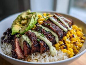 Close-up of a steak avocado and roasted corn bowl with seasoned steak slices over rice and drizzled with creamy sauce.