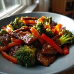 Close-up of glossy sticky orange beef stir fry mixed with bright green broccoli florets and red bell pepper strips.