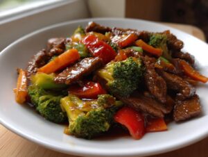 A close-up of a white bowl filled with sticky orange beef stir fry, featuring tender beef strips, bright green broccoli, and orange carrots.