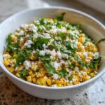 Close-up of a white bowl filled with vibrant street corn salad topped with crumbled white cheese and fresh cilantro.