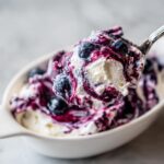 A spoonful of creamy blueberry fluff salad, showing swirls of purple blueberry sauce mixed into the white whipped topping.