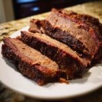 Close-up of several thick slices of tender, smoked beef brisket showing a deep red smoke ring and dark spice rub bark.