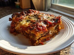 A close-up, sunlit slice of baked Eggplant parmesan layered with cheese and rich tomato sauce.