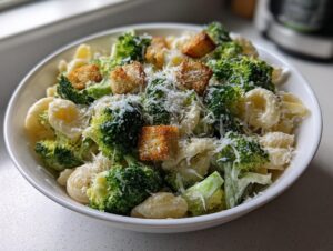 A close-up of a bowl filled with Broccoli caesar pasta salad, featuring pasta, bright green broccoli florets, croutons, and grated Parmesan cheese.