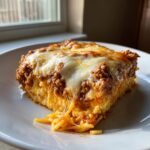 A square slice of Leftover spaghetti bake with melted, stringy cheese and rich meat sauce on a white plate.