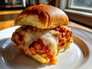 Close-up of a single, delicious chicken parmesan sliders topped with melted mozzarella cheese and marinara sauce.