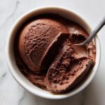Overhead view of rich, dark chocolate cottage cheese mousse scooped into a white bowl with a spoon.