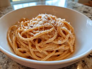 Close-up of creamy Carbonara buldak ramen noodles topped with grated cheese and black pepper in a white bowl.