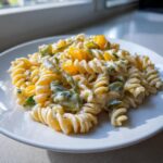 Close-up of creamy Dill pickle pasta salad made with rotini pasta, green pickle pieces, and yellow bell pepper chunks.