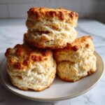 Close-up of three tall, flaky buttermilk biscuits stacked on a small plate, showing their layered texture.