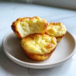 Three fluffy Cottage cheese egg bites served on a small plate, one is bitten into showing the light interior.
