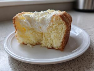 Close-up of a fluffy slice of yellow Daffodil cake topped with white whipped cream, served on a white plate.