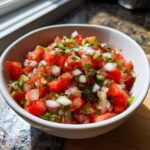 Close-up of fresh, chunky Pico de Gallo made with diced tomatoes, white onion, and cilantro in a white bowl.