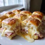Close-up of gooey, melted Ham and Cheese Sliders topped with poppy seeds, showing cheese stretching between the rolls.
