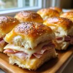 Close-up of gooey Hawaiian roll sliders filled with ham and melted Swiss cheese, topped with poppy seeds.