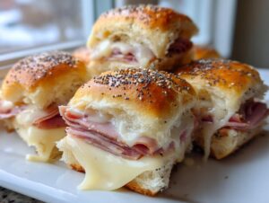 Close-up of several gooey Hawaiian roll sliders filled with ham and melted cheese, topped with poppy seeds.