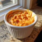 A close-up shot of hot, creamy Buffalo chicken dip served in a white ramekin, glistening with melted cheese.