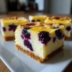 A close-up of a thick, square slice of Lemon blueberry cheesecake bars showing the creamy filling, bright blueberries, and graham cracker crust.