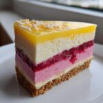 A perfect slice of Lemon Raspberry Cheesecake showing distinct layers of crust, pink mousse, white filling, and bright yellow lemon topping.