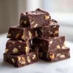 A tempting stack of rich, dark Nutty chocolate fudge squares generously studded with visible pieces of walnuts.
