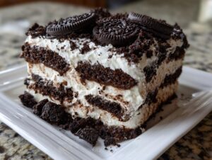 A decadent slice of Oreo icebox cake showing layers of chocolate cookies and whipped cream, topped with crushed Oreos.