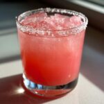 Close-up of a vibrant pink Rhubarb margarita served on the rocks with a coarse salt rim.