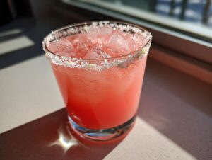 Close-up of a bright pink Rhubarb margarita cocktail served over ice with a thick salt rim.
