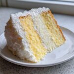 A tall, perfect slice of Daffodil cake showing alternating yellow sponge and white filling/frosting layers on a white plate.